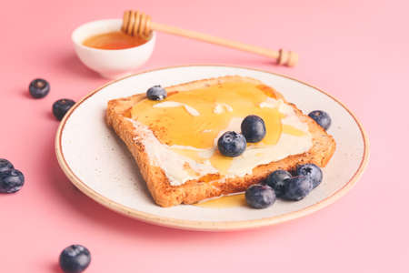 Tasty toasted bread with honey, butter and berries on color backgroundの写真素材