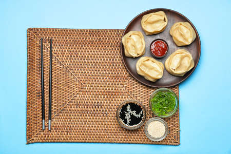 Plate with oriental dumplings and sauces on color background