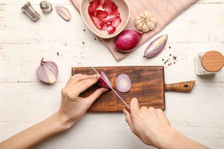 Woman cutting fresh raw onion on wooden background, top viewの写真素材