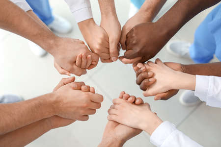 Group of doctors putting hands together in clinic. Unity concept