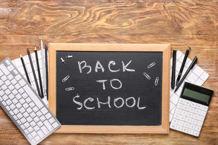 Set of supplies, computer keyboard and chalkboard with text BACK TO SCHOOL on wooden background