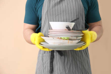 Young man with dirty dishes on color background, closeupの写真素材
