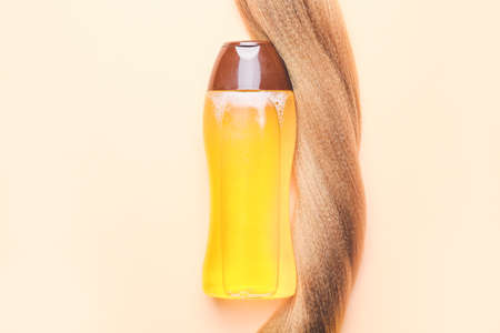 Bottle of shampoo and hair strand on color backgroundの写真素材