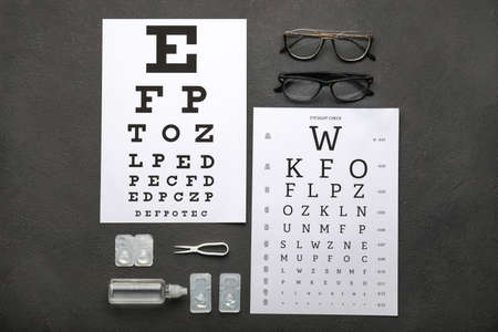 Eye test charts with eyeglasses, containers for contact lenses, solution and tweezers on dark backgroundの写真素材