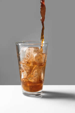 Pouring of coffee into in glass with ice cubes on tableの写真素材