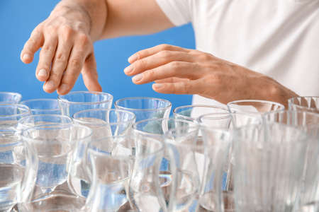 Young man playing music on glasses with water against color background, closeup