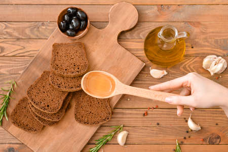 Woman pouring tasty olive oil from spoon on fresh breadの写真素材