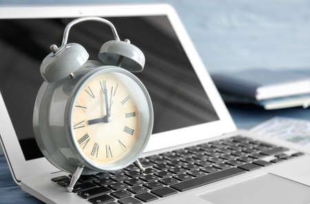 Alarm clock with laptop on table, closeup. Time management conceptの写真素材