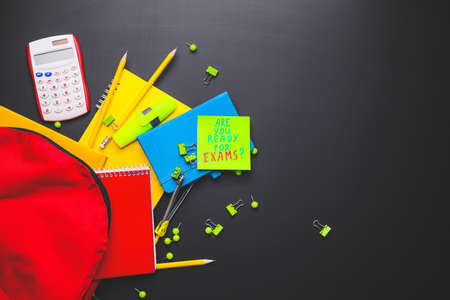 Backpack, stationery and paper sheet with text ARE YOU READY FOR EXAMS? on dark backgroundの写真素材