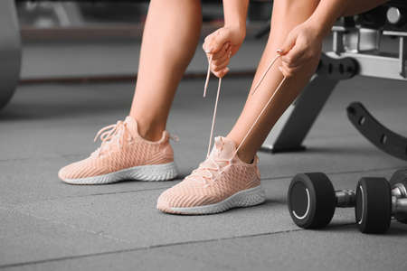 Sporty young woman tying shoelaces in gymの写真素材