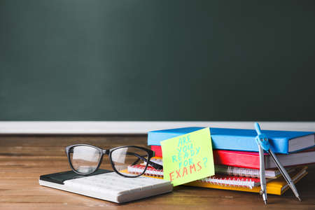 Stationery and paper sheet with text ARE YOU READY FOR EXAMS? on table in classroomの写真素材