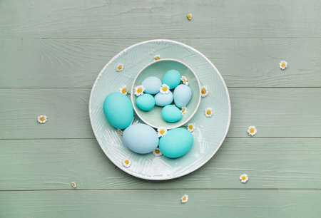 Plate with beautiful Easter eggs and flowers on wooden background