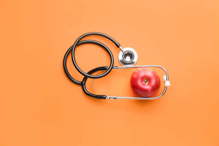 Fresh apple and stethoscope on color background
