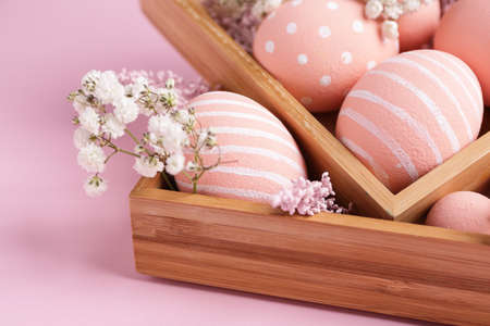 Boxes with beautiful Easter eggs and flowers on color background
