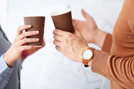 Young colleagues drinking coffee in office, closeupの写真素材