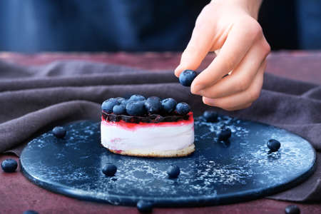 Female confectioner decorating tasty cake on table, closeupの写真素材