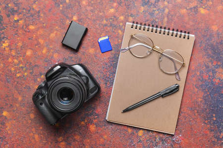 Modern photo camera with notebook, pen and eyeglasses on color backgroundの写真素材