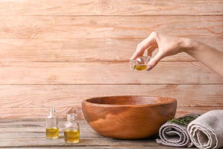 Woman pouring essential oil from bottle into bowl on wooden backgroundの写真素材