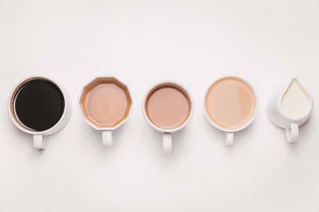 Cups of different coffee and jug with milk on light backgroundの写真素材