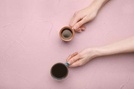 Female hands with cups of coffee on color backgroundの写真素材