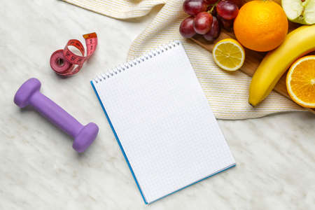 Notebook with healthy products, measuring tape and dumbbell on tableの写真素材