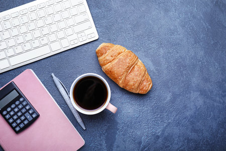 Cup of coffee with croissant, computer keyboard, calculator and notebook on dark backgroundの写真素材
