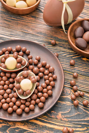 Plate with chocolate eggs and candies on wooden tableの写真素材