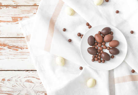 Plate with chocolate eggs and candies on wooden tableの写真素材