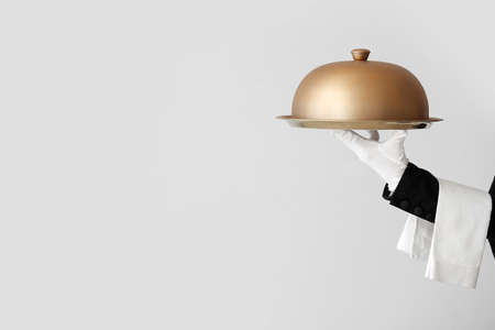 Hand of waiter with tray and cloche on gray background