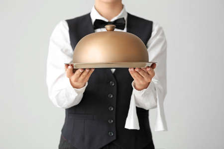 Beautiful female waiter with tray and cloche on gray backgroundの写真素材