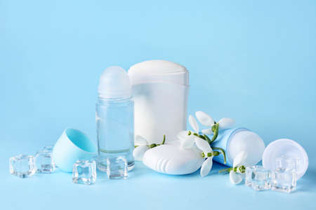 Different deodorants and flowers on color background