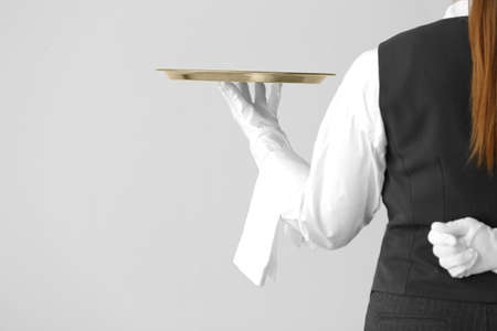 Beautiful female waiter with empty tray on gray backgroundの写真素材