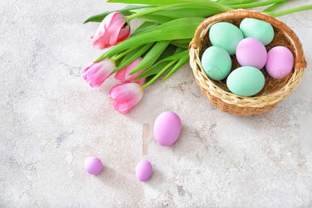 Basket with beautiful Easter eggs and flowers on light backgroundの写真素材