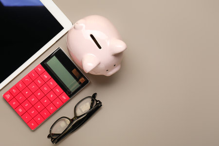 Calculator with piggy bank, tablet computer and eyeglasses on gray backgroundの写真素材