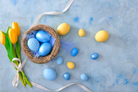 Nest with beautiful Easter eggs and flowers on color backgroundの写真素材