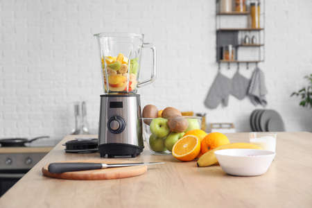 Modern blender with fresh fruits and cutting board on table in kitchenの写真素材