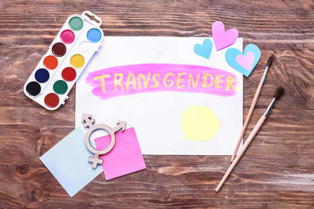 Paper sheet with word TRANSGENDER, paints and brushes on wooden backgroundの写真素材