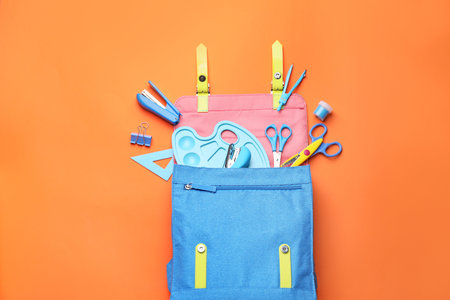 School backpack and stationery on color background