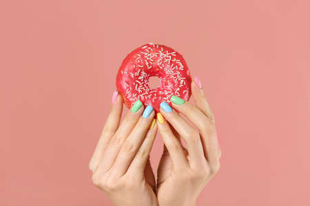 Hands of young woman with beautiful manicure and donut on color backgroundの写真素材