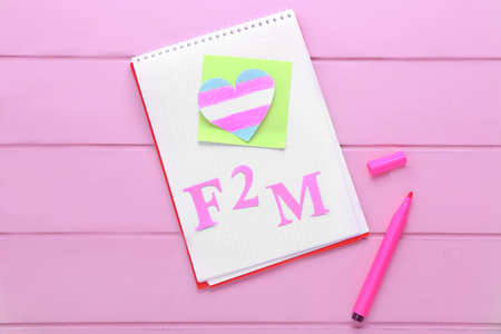 Notebook with paper heart and abbreviation F2M on color wooden background. Concept of transgenderの写真素材