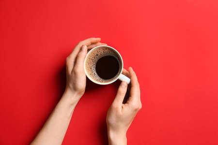 Female hands with cup of hot coffee on color backgroundの写真素材