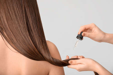 Applying of cosmetics on woman's hair against gray backgroundの写真素材