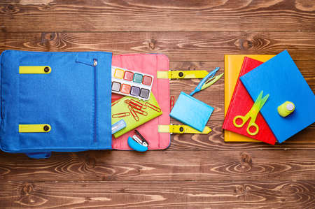 School backpack and stationery on wooden background