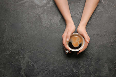 Female hands with cup of hot coffee on dark backgroundの写真素材
