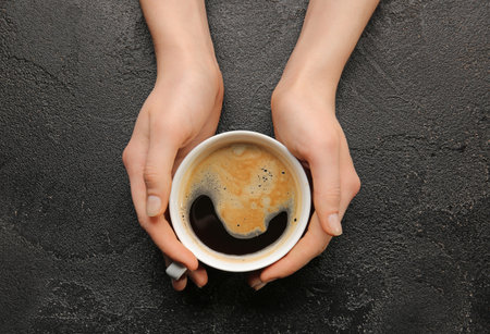 Female hands with cup of hot coffee on dark backgroundの写真素材