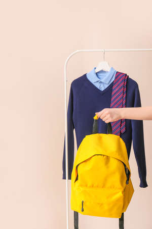 Stylish school uniform hanging on rack and female hand with backpack against color backgroundの写真素材