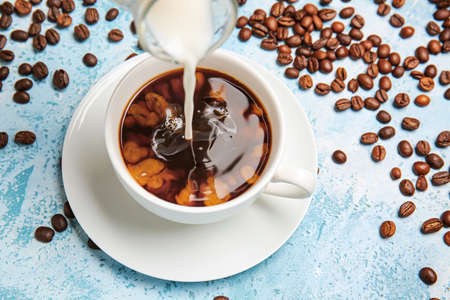 Pouring of milk in cup of hot coffee on tableの写真素材