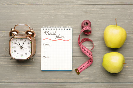 Meal plan with measuring tape, alarm clock and apples on table