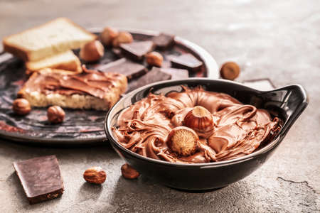 Bowl with tasty chocolate paste and hazelnuts on grunge background