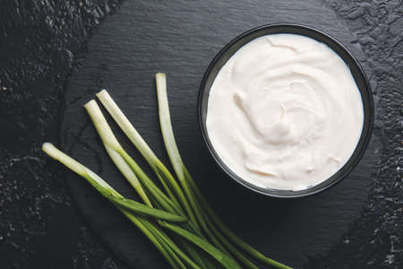Bowl with tasty sour cream and green onion on tableの写真素材